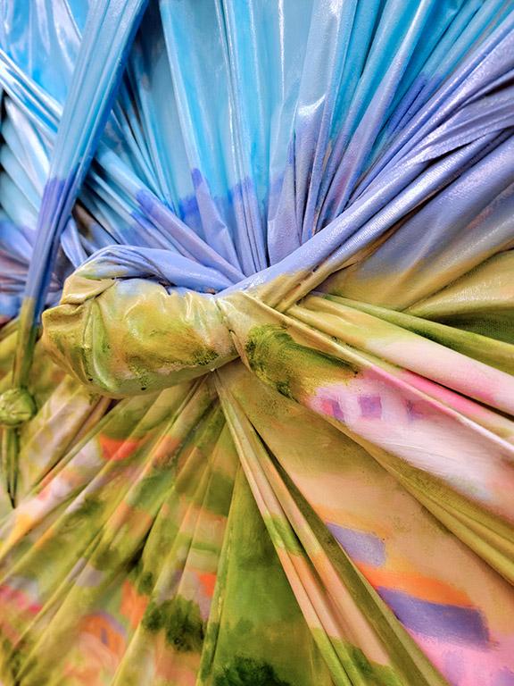 Plastic sheeting is cinched and knotted on top of a canvas, with a landscape painting on top of the sheeting.