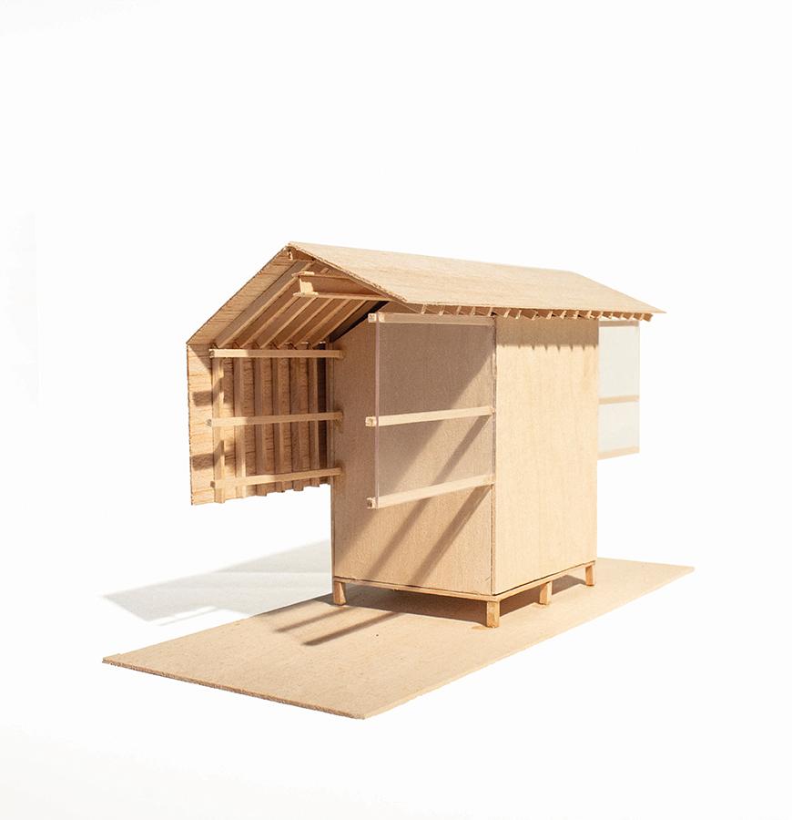 Wooden model of a house with an extended roof offering a sheltered porch.