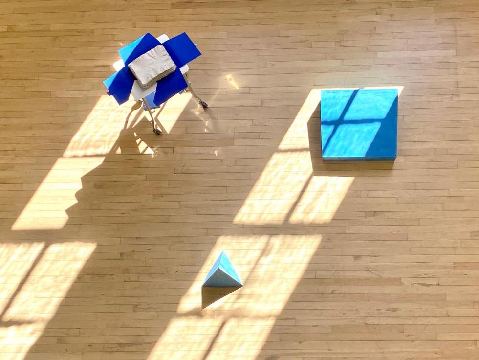Overhead view of a gallery with blue geometric sculptures on the wood floor.