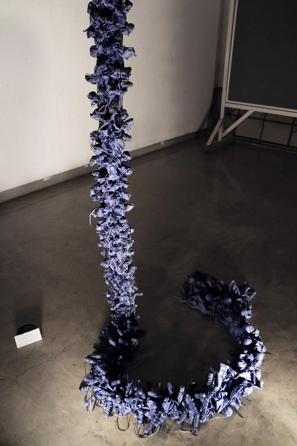 A long chain of blue cloth pieces hangs from the ceiling and coils on the floor.