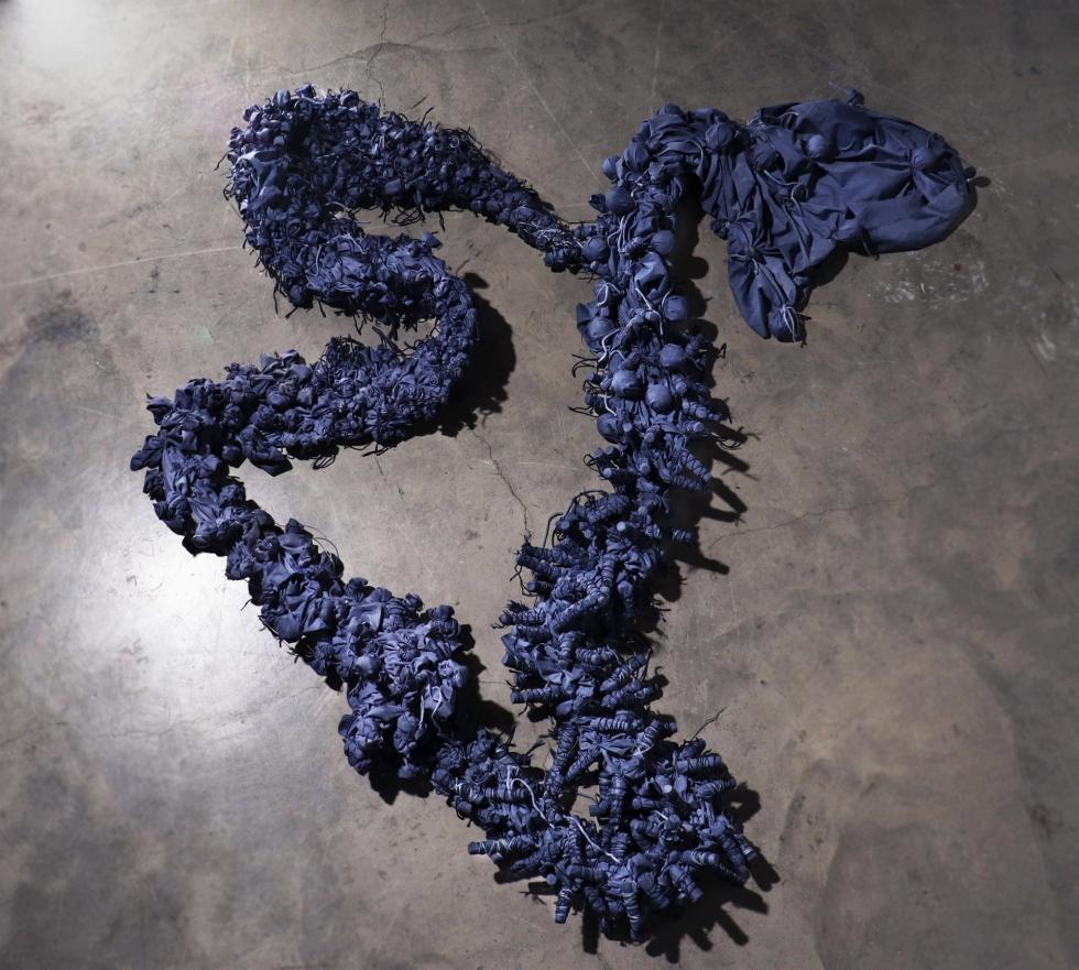 A long chain of blue cloth pieces coils on the floor.