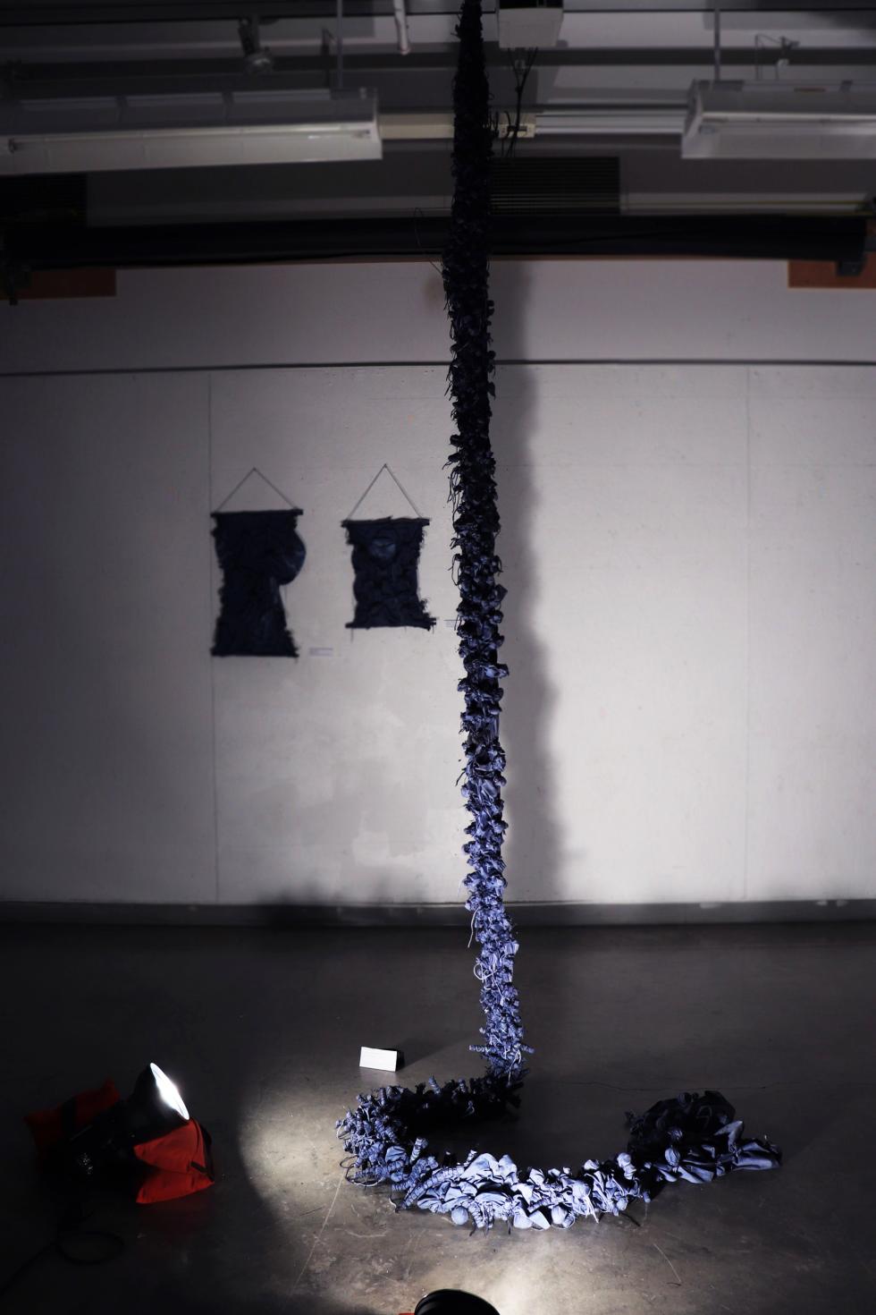 A long chain of blue cloth pieces hangs from the ceiling and coils on the floor.