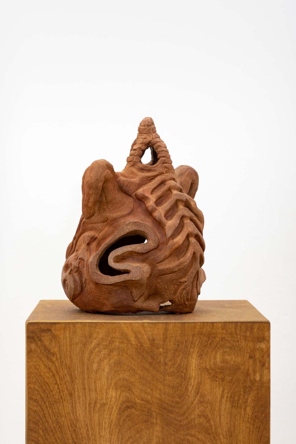 A wooden pedestal with an abstract clay sculpture.