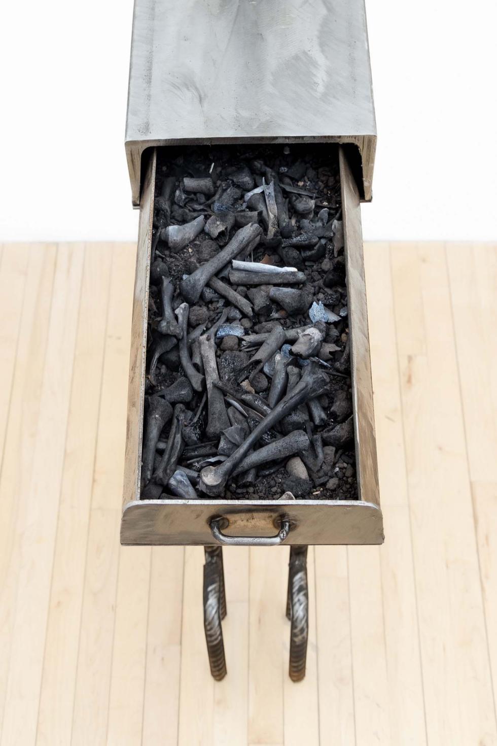 A steel table with one small drawer. Inside the drawer are a lot of burnt chicken bones.