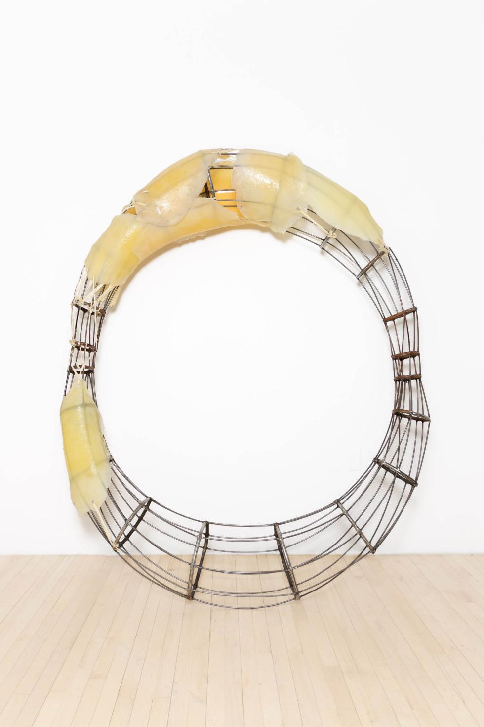 A steel circular sculpture with silicone slabs attached to parts of it.
