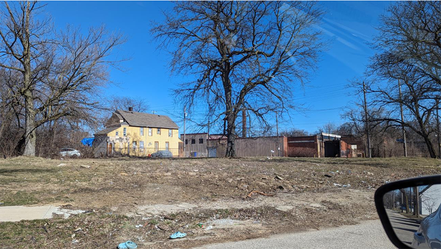Yellow house with unmaintained landscaping and a series of wooden and metal sheds next to it.