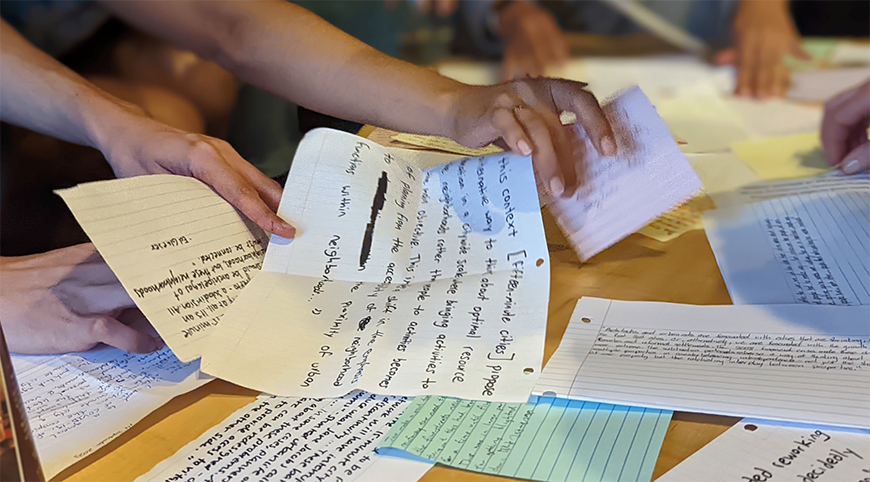 Hands sort through hand written notes scattered on a table.