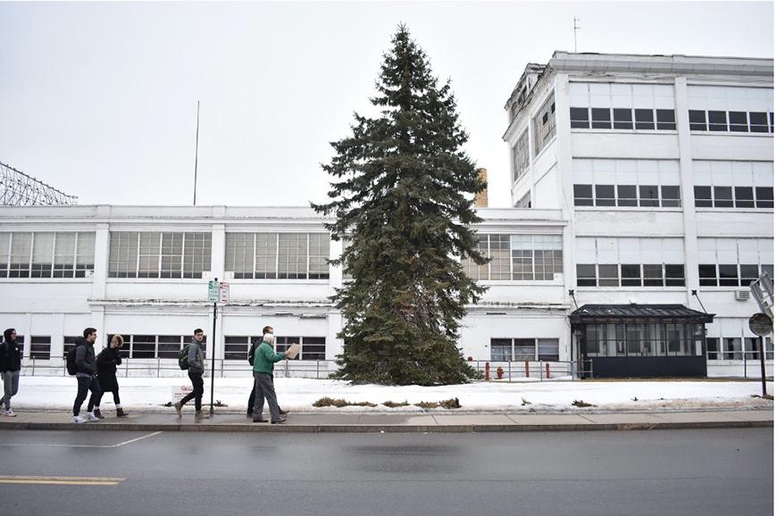 A group of people walk along a sidewalk with snow on the ground and a white building in the background.