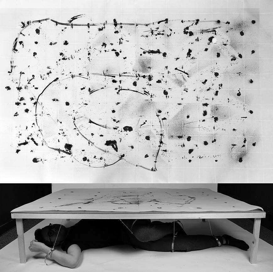 A grid if many ink splatters and lines, with an image of a person using wires connected to their body to influence these ink splatters.