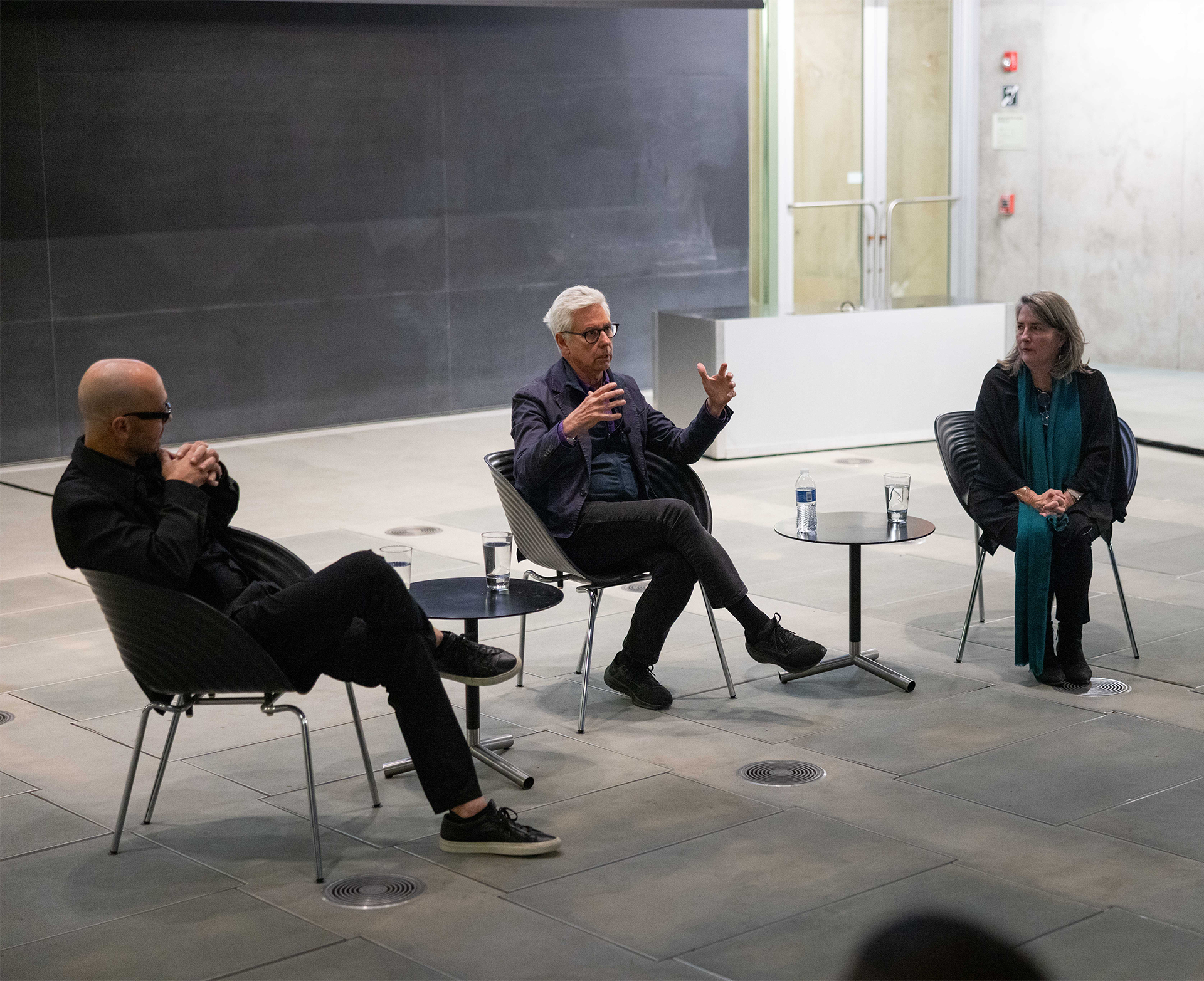 Three people sit at the front of an auditorium and address an audience.
