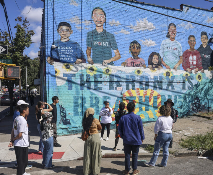 Group of people look at a mural on a brick wall that says 