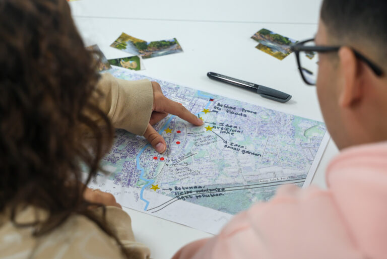 Two people look at a map on a table and the map has written notes on it.