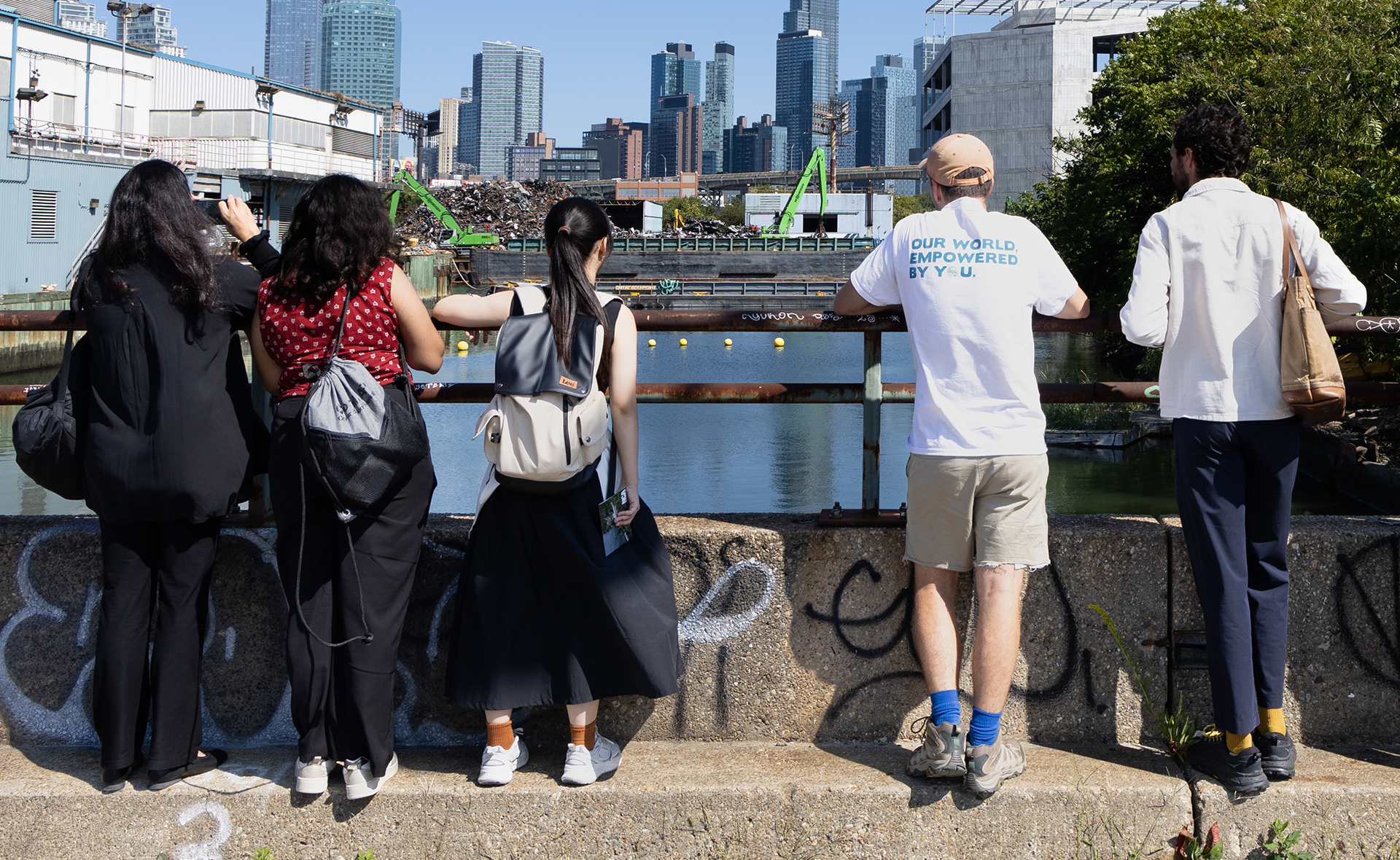 Five people stand on a bridge overlooking a cityscape.