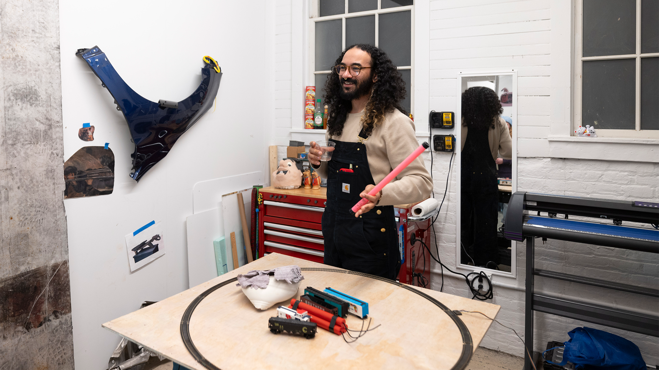 A person gives a tour of their art studio with art on the wall and a tool box positioned behind them.