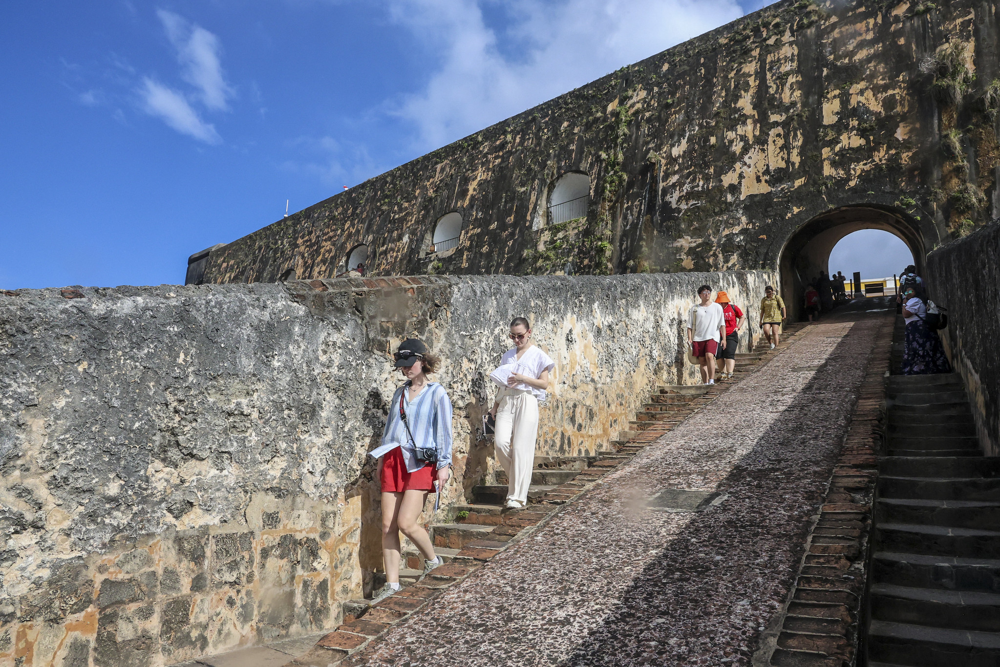 People walk down an outdoor staircase lined with a tall stone wall.