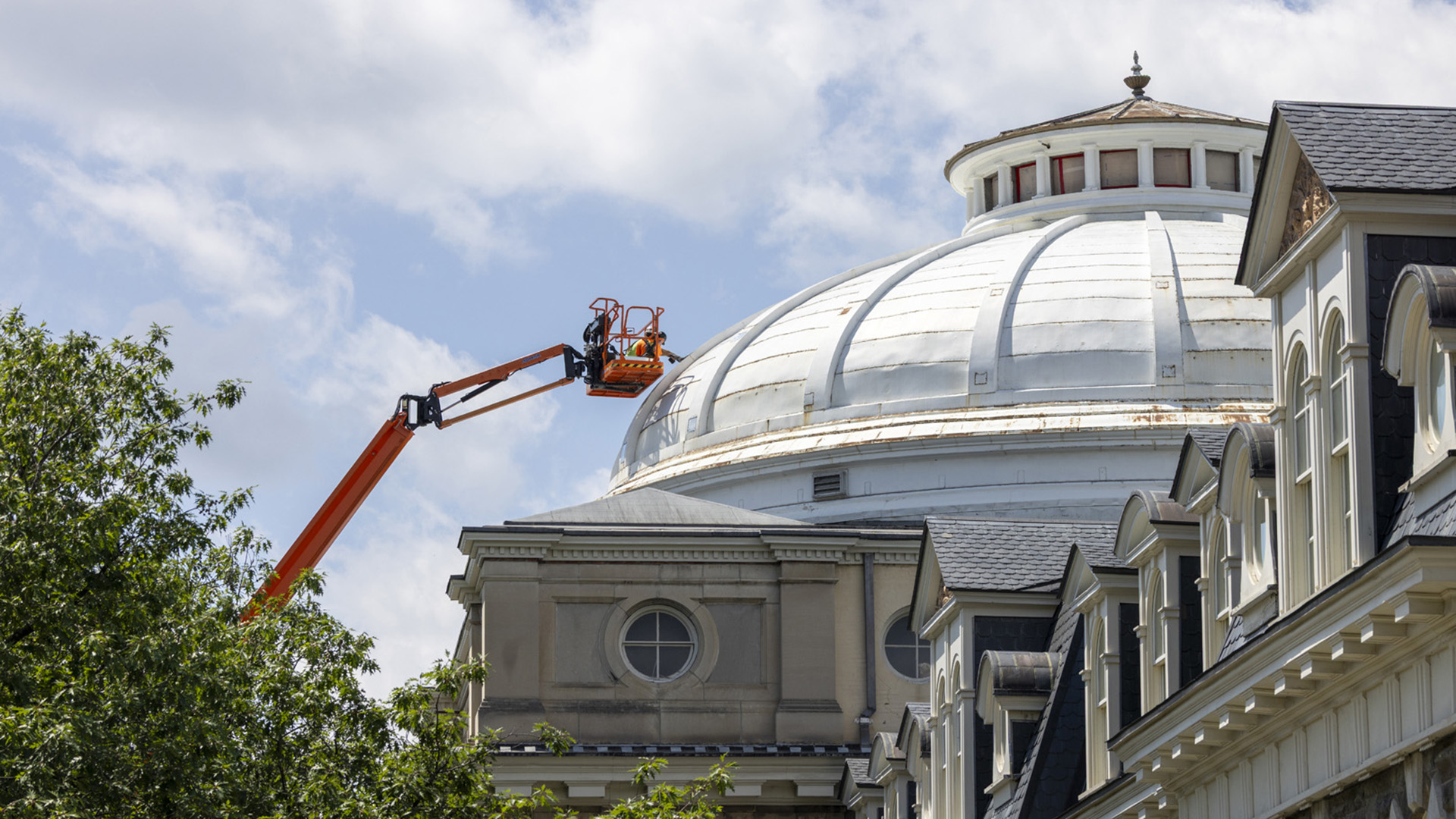 Exterior of a building with a white dome and a crane holding two construction workers.