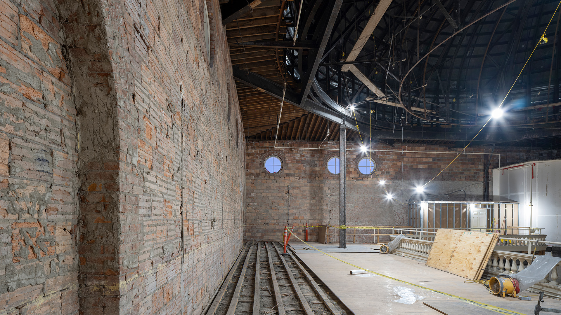 Interior of a brick building with circular windows at one end and building materials stacked on the right side.