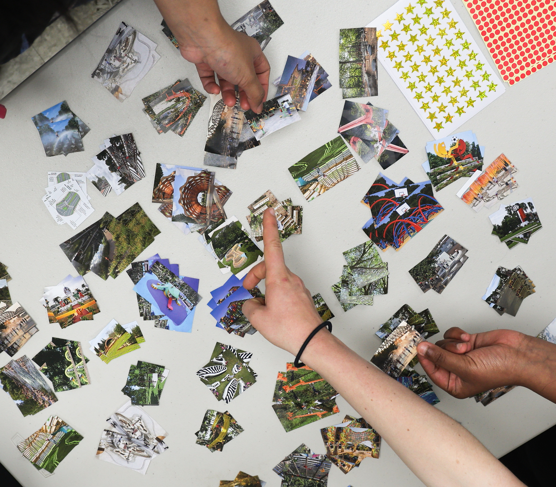 The hands of three people are sorting small cutout images on a white table.