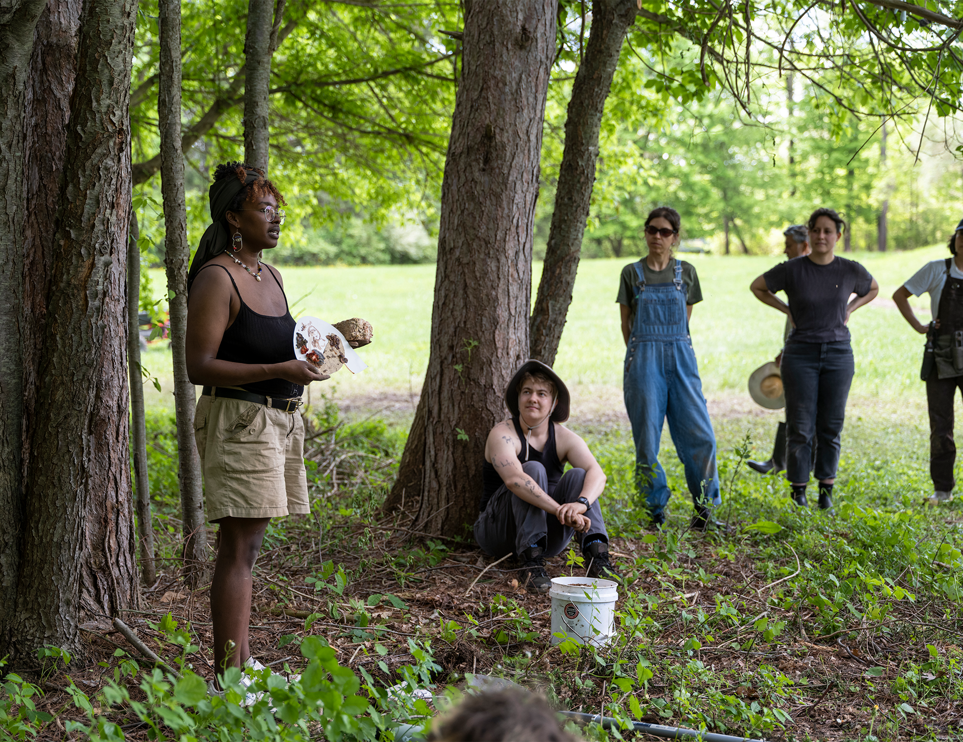 People gather in a forest and listen to a presentation.