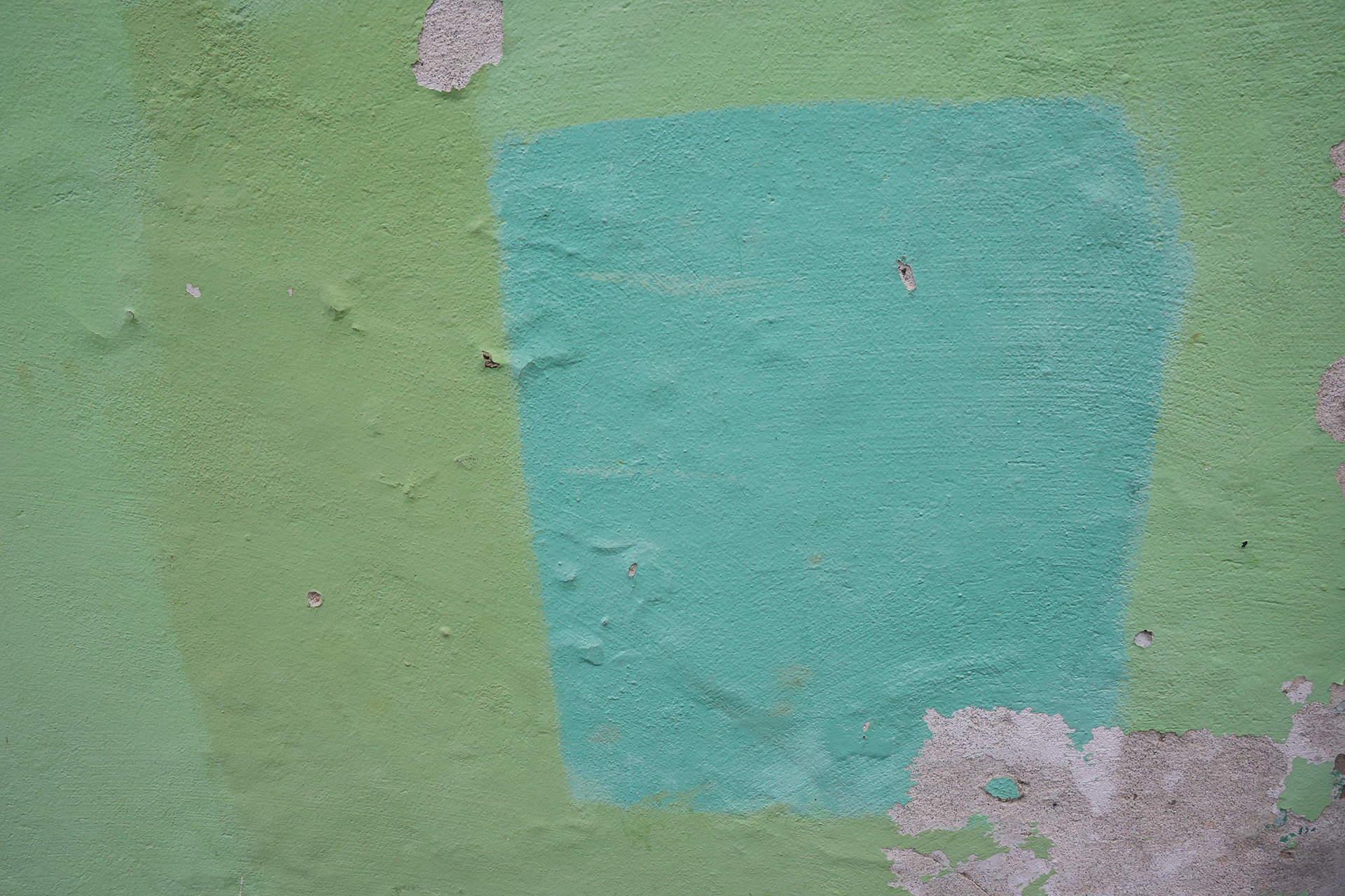 A painted concrete wall with blue and green color blocks and peeling paint in the bottom right corner.