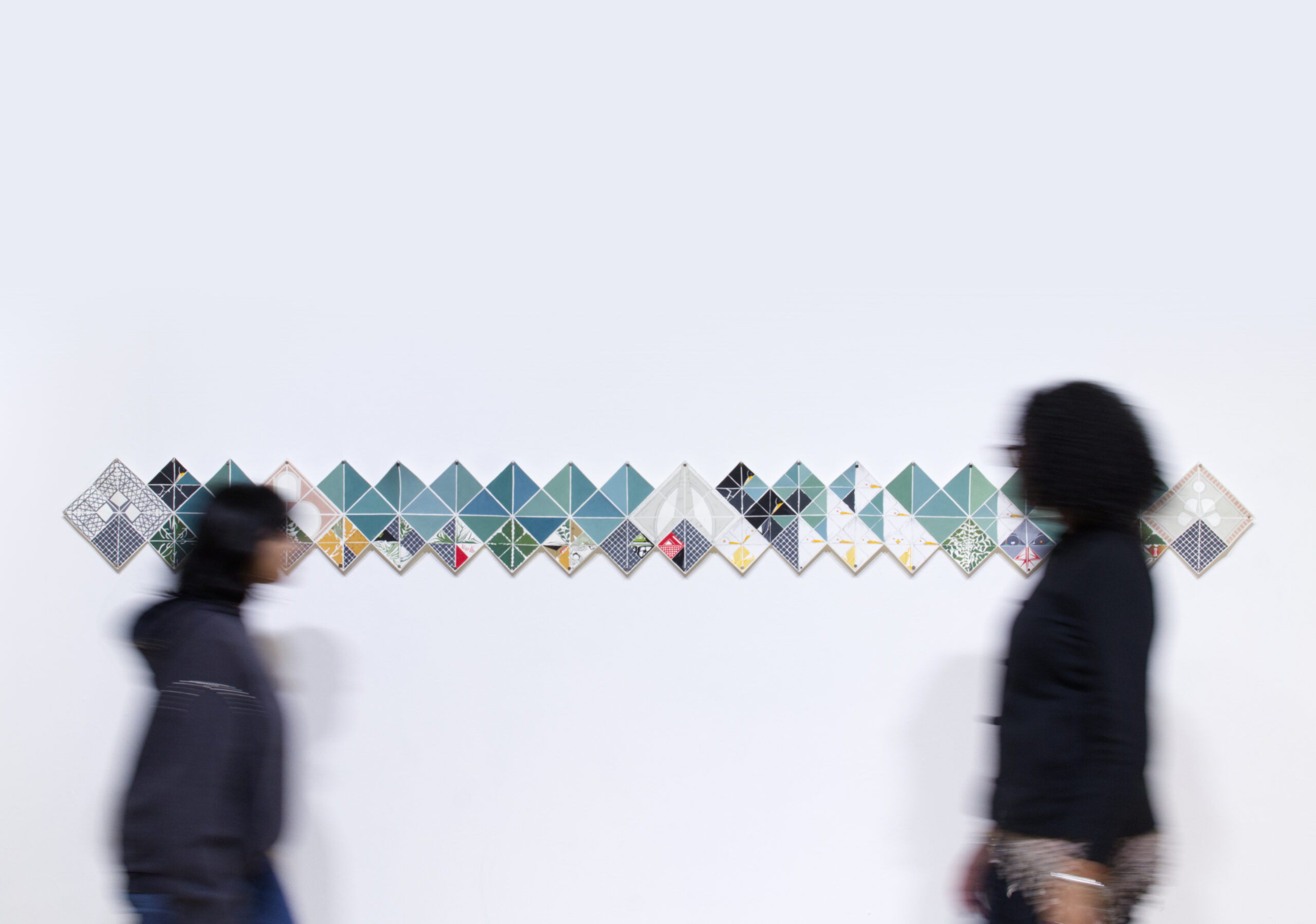 Two people look at a white wall with a series of triangular panels in a line.