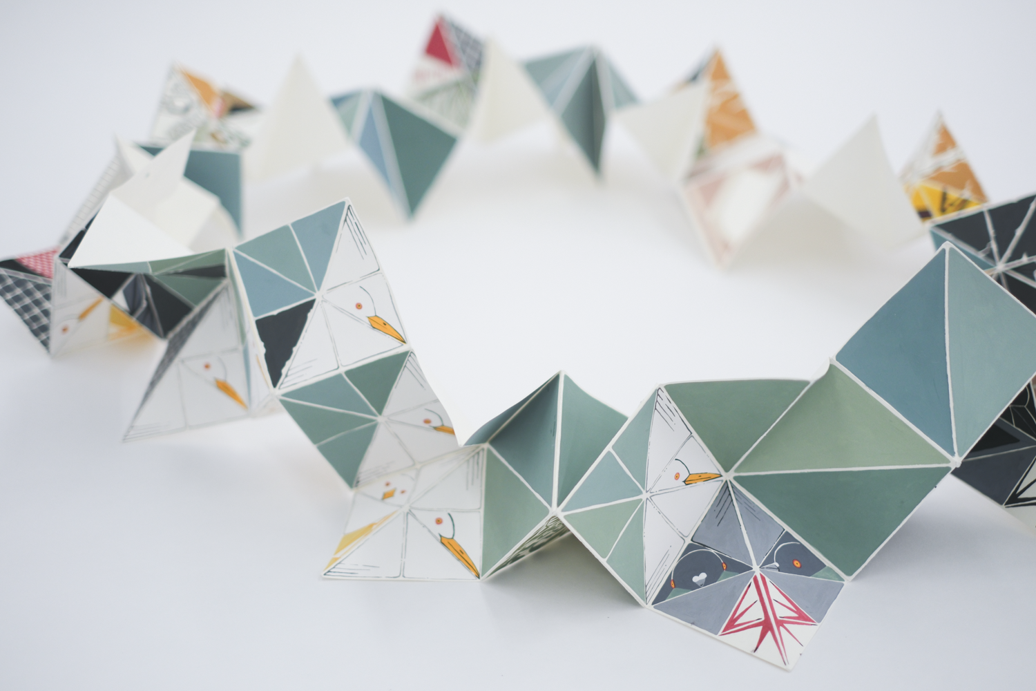 A long sheet of paper is folded into triangles that are colored with shades of green and blue.