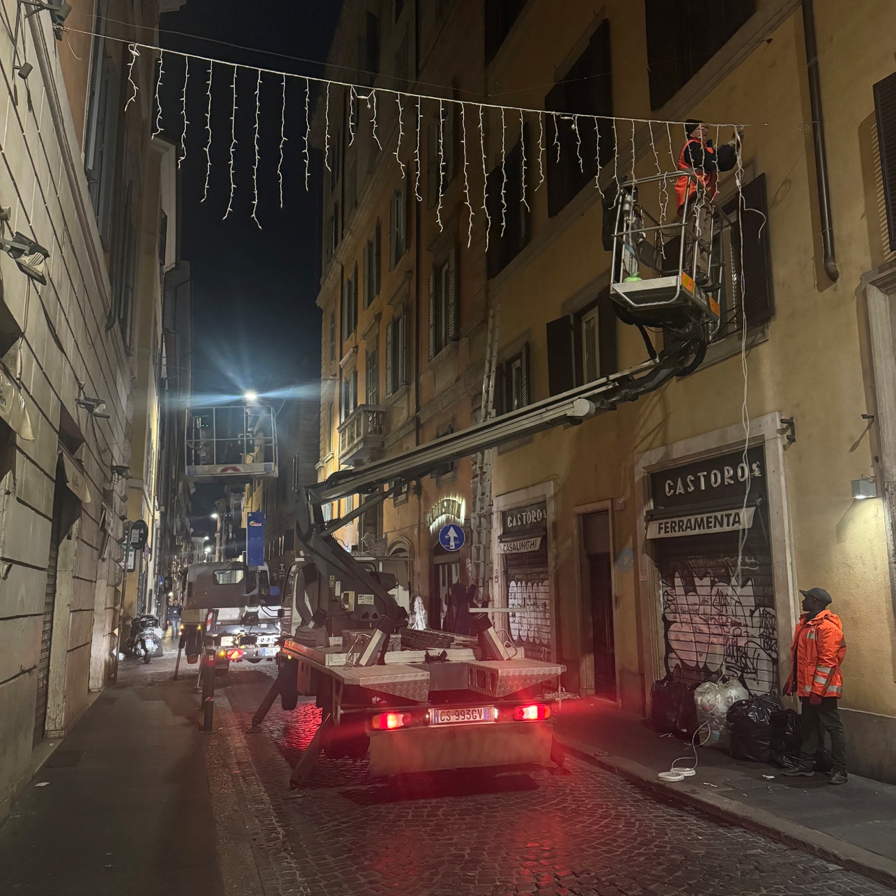 A city street at nighttime with a car in the middle of the road and its brake lights are on.
