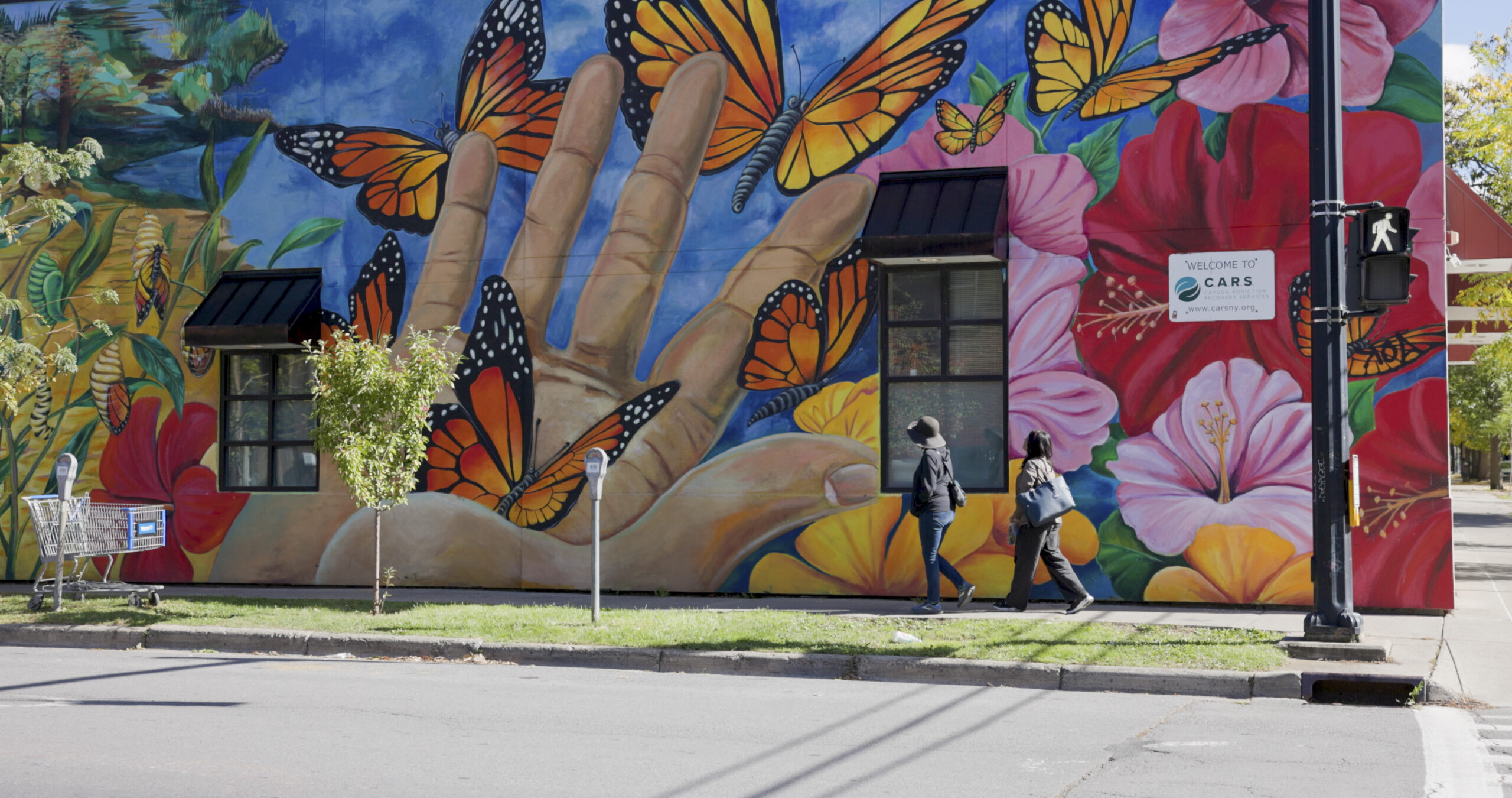 two people walking in front of an urban mural with butterflies