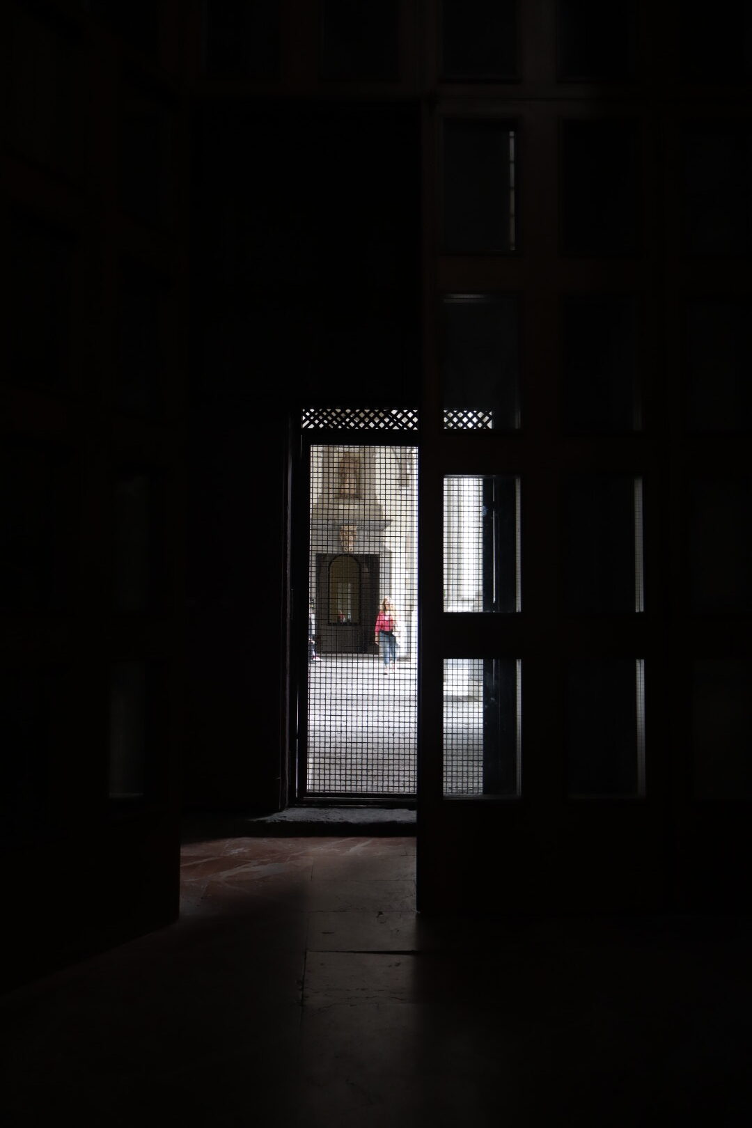 a person walking, a mesh doorway, and building facade as seen from a dark room