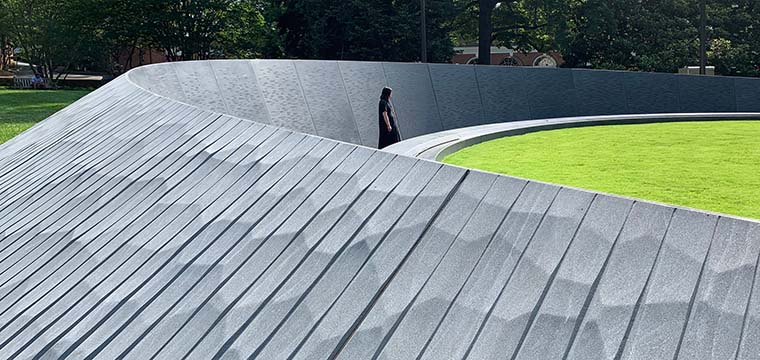 A person walks along a stone structure with grass.