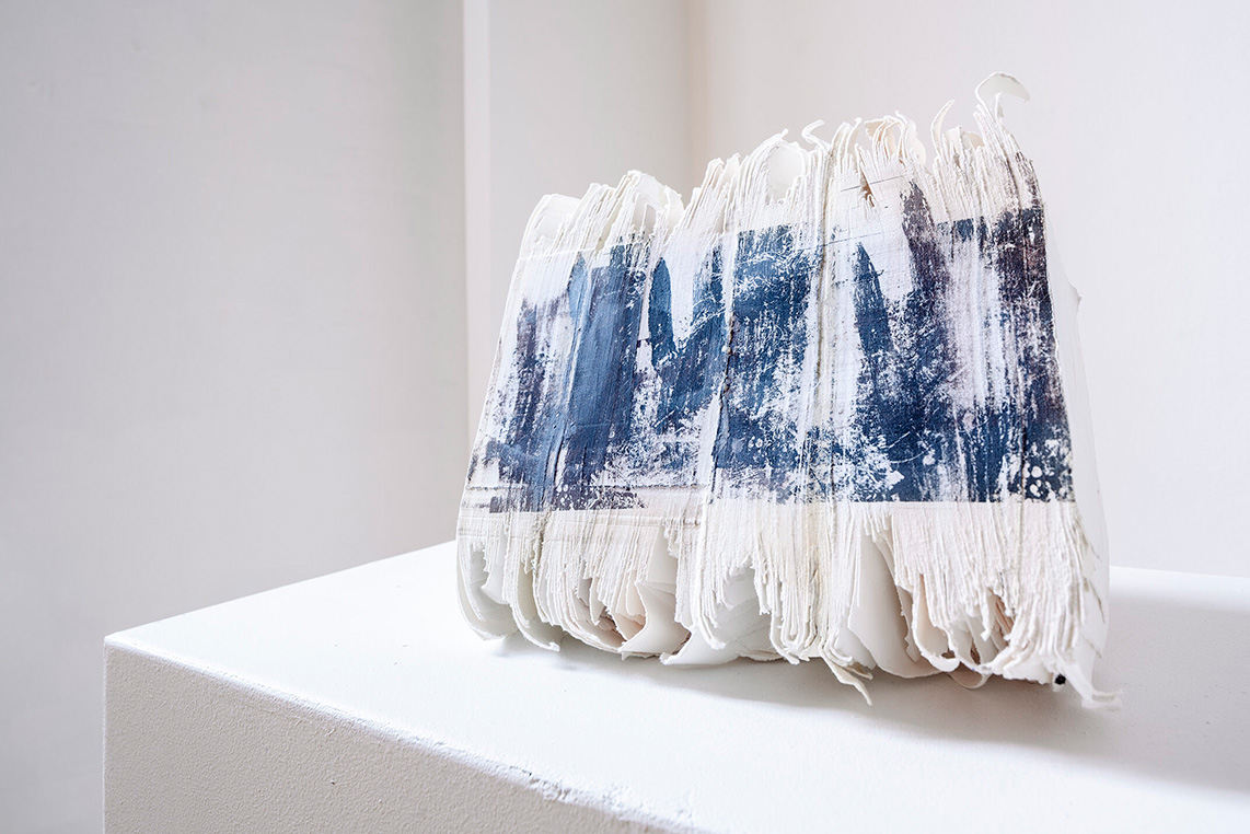 Handmade paper pages are pressed together in a large stack, with an ink imprinting on the side of the stack.