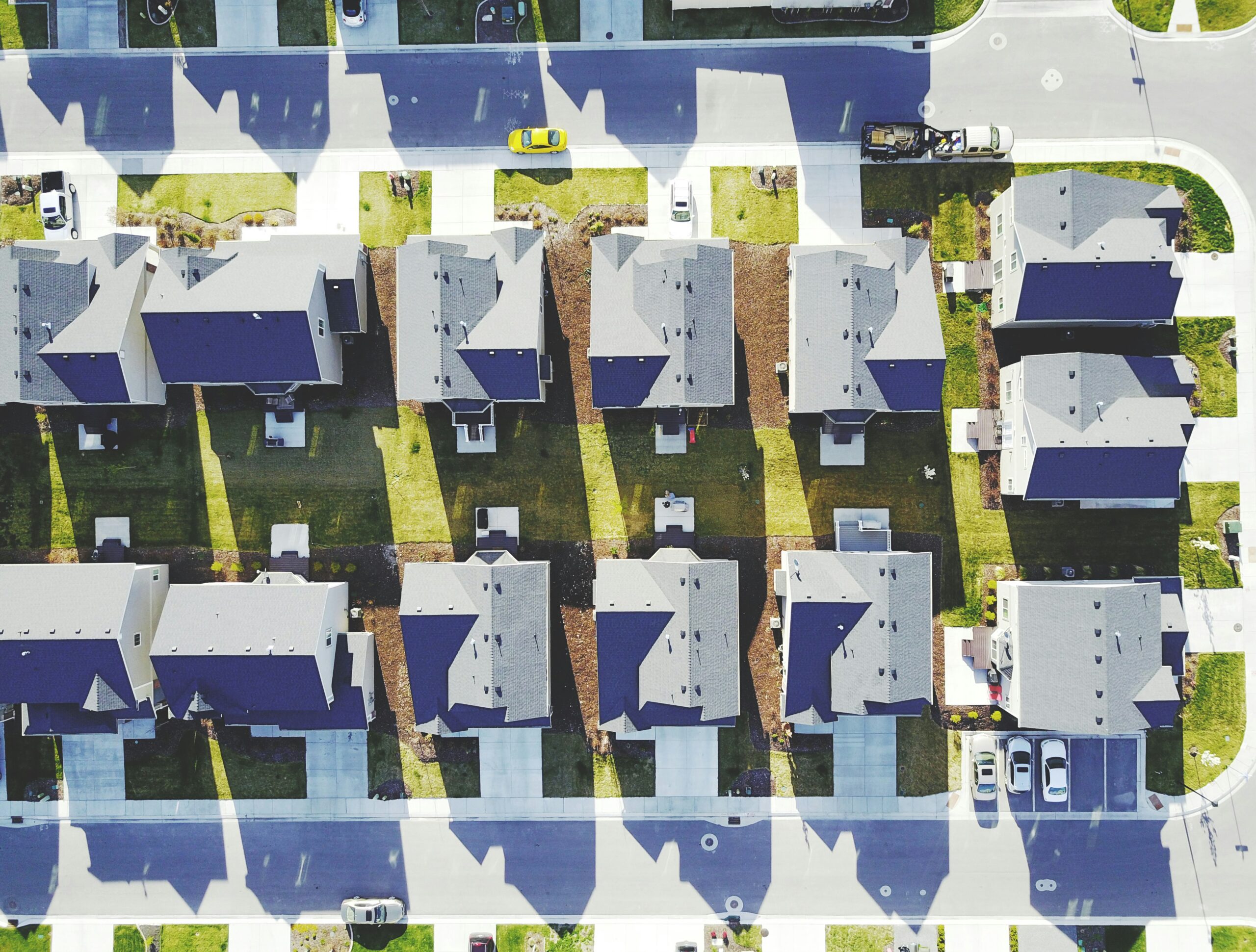 Aerial view of a suburban neighborhood with evenly spaced single-family homes, driveways, and green yards casting long shadows across the streets.