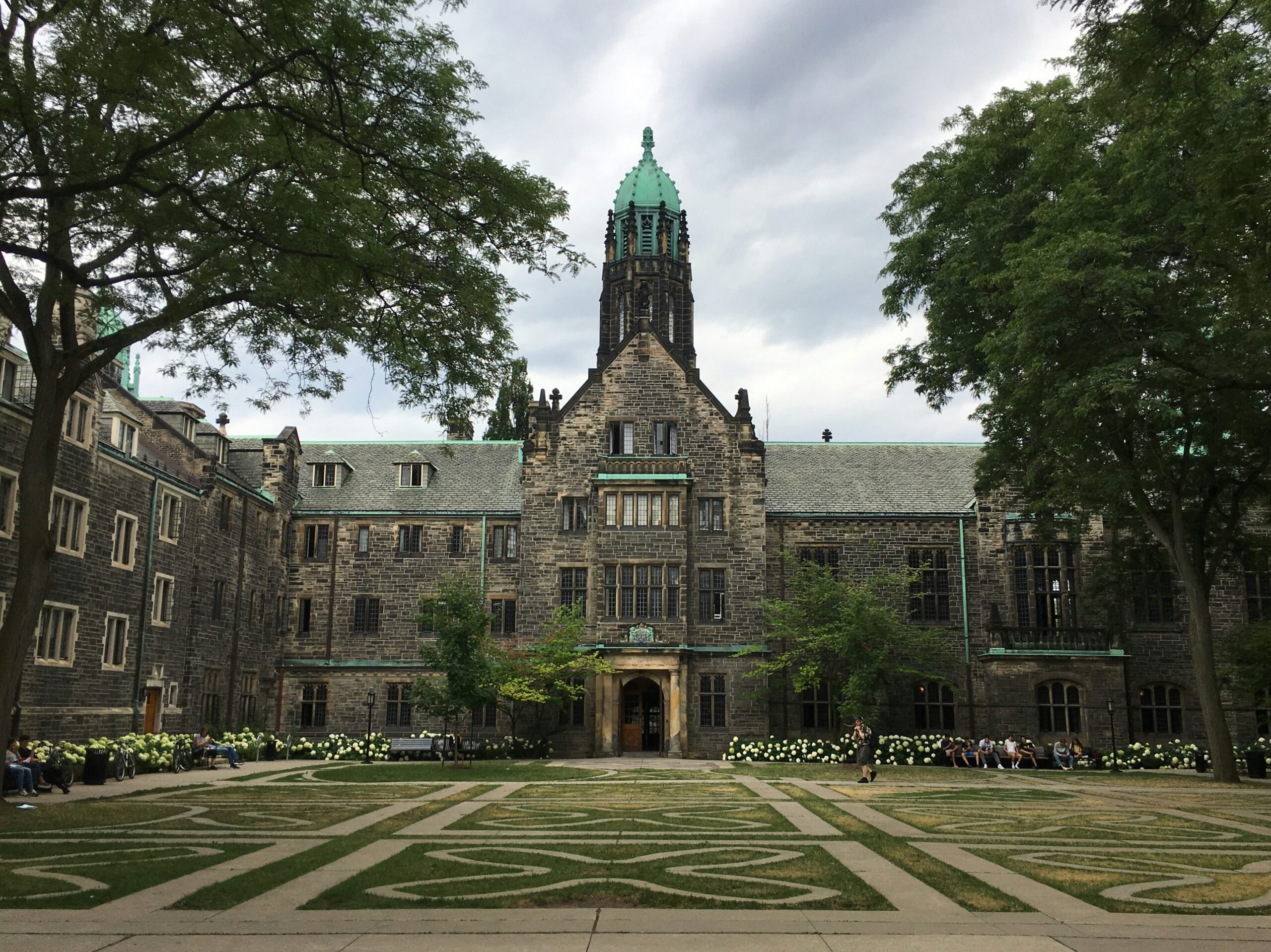 A stone, gothic style university building surrounded by a highly manicured lawn.