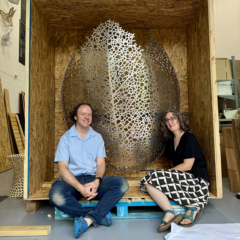 two people sitting in a shipping container box with a large object behind them within the box.