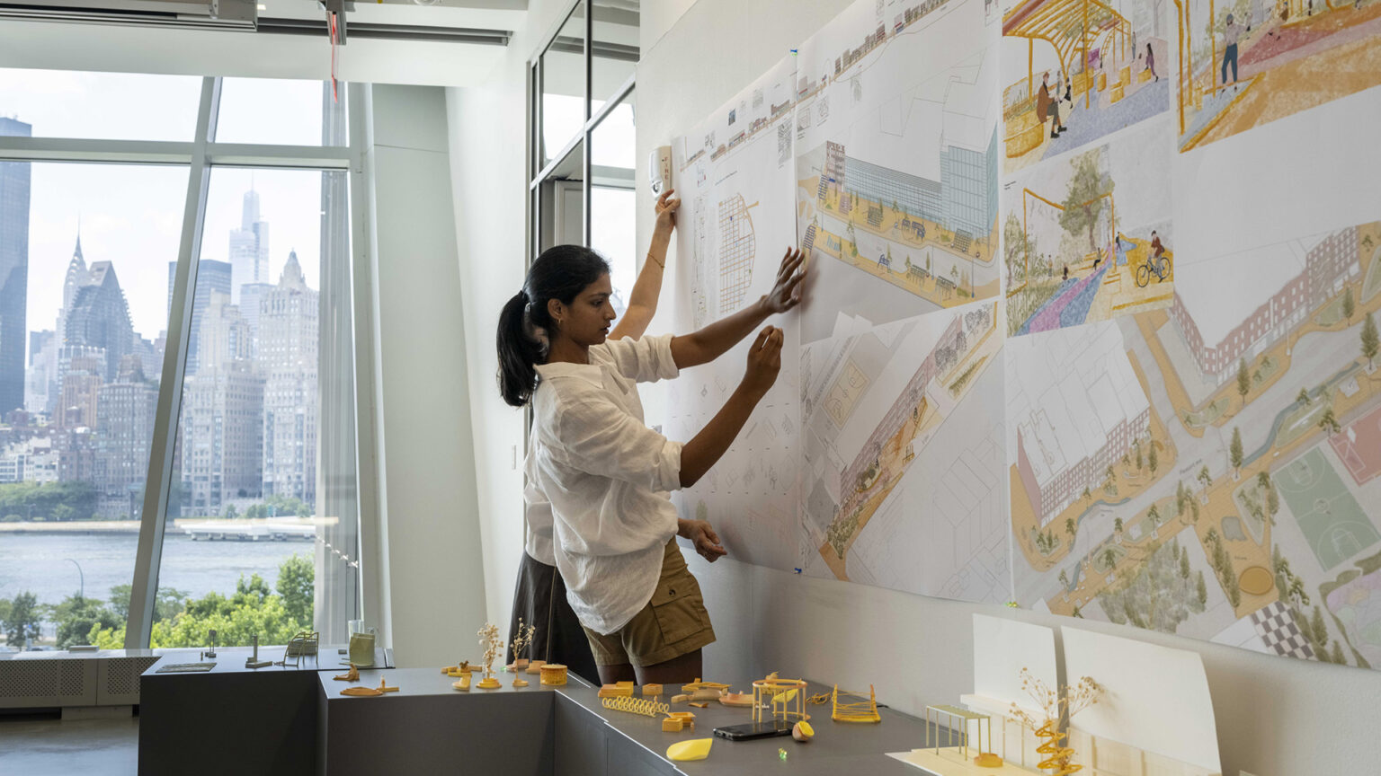 a person pins up content on a wall with a city scape in the window.