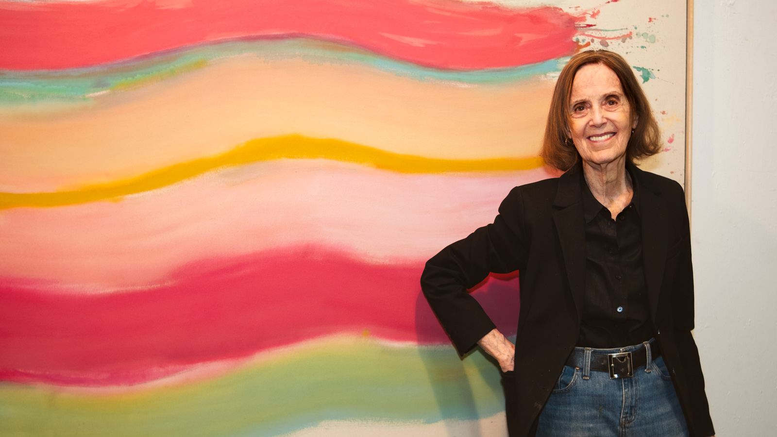 Woman standing in front of brightly painted canvas.