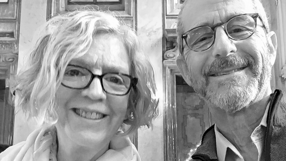 Two people with their heads close together posing in an ornate room.