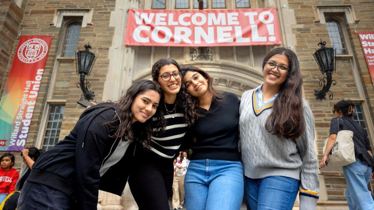 Four people smile and pose together under a welcome to Cornell banner.