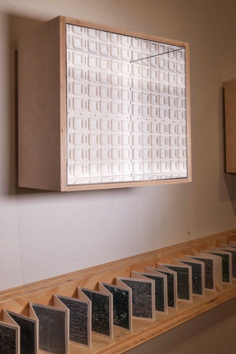 a wooden case with glass hung on a wall with a wooden ledge containing a zig zag folded photostrip