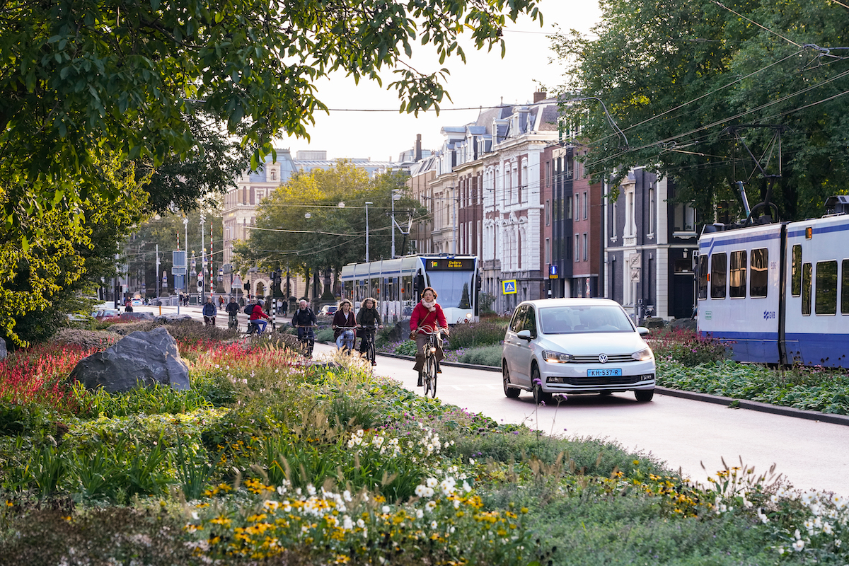 Amsterdam street with green public space, bicycles, and a tram in the background