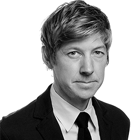 A black-and-white headshot of Jesse LeCavalier in a suit and tie, looking slightly off-camera with a neutral expression against a white background.