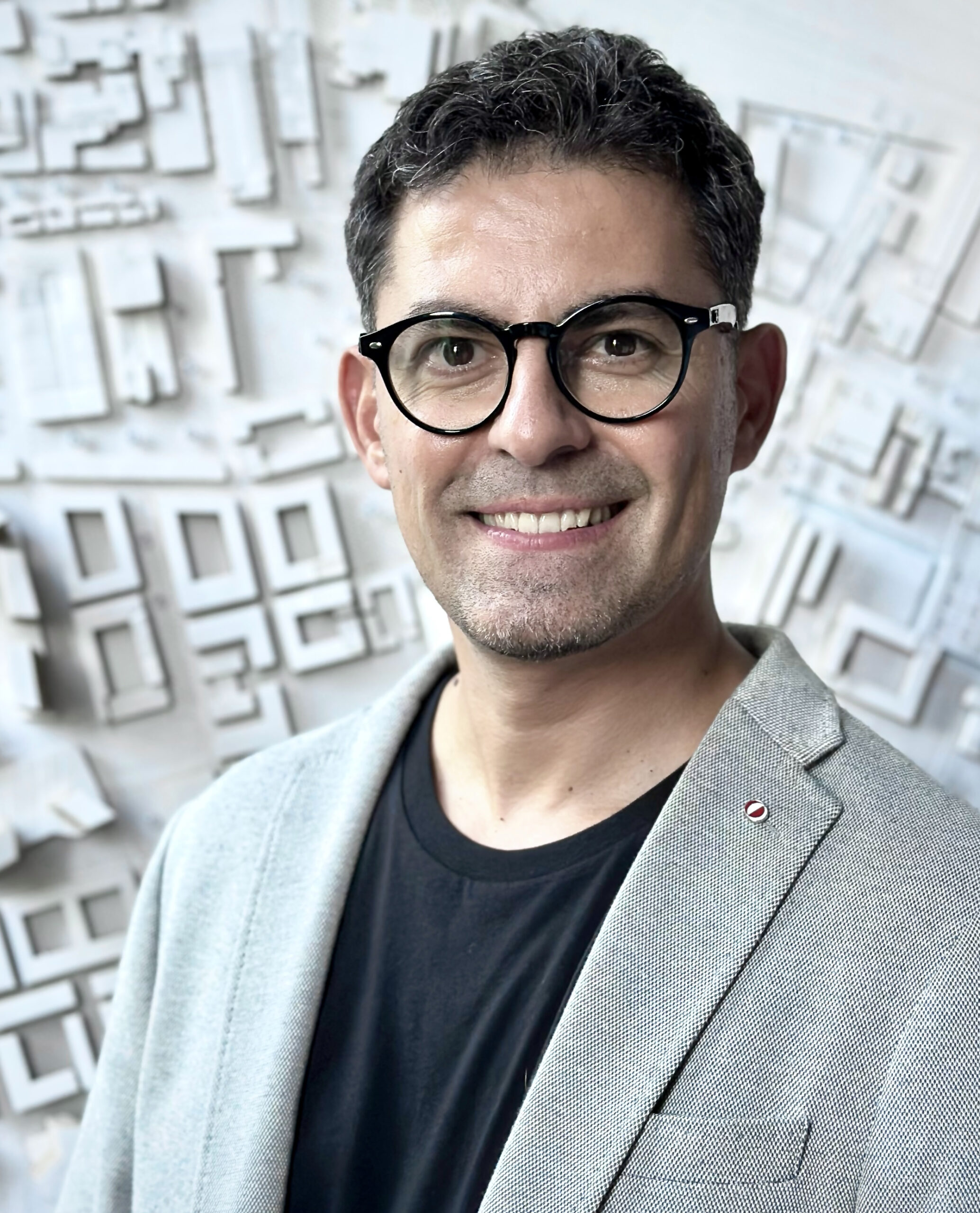 Headshot of architect Olgu Çalışkan wearing glasses with a white architectural model in the background.