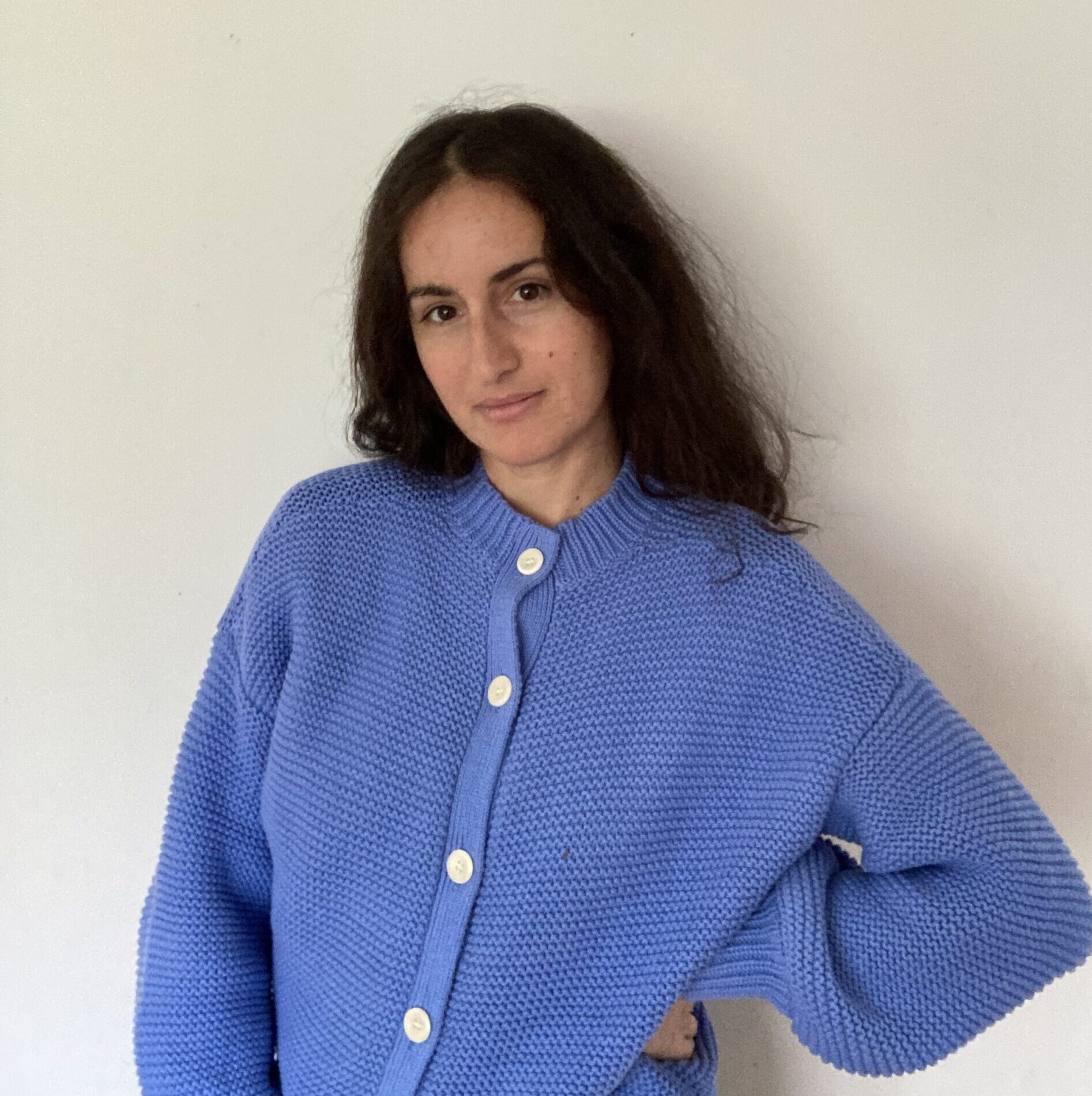 A woman with long dark hair, wearing an oversized blue sweater.