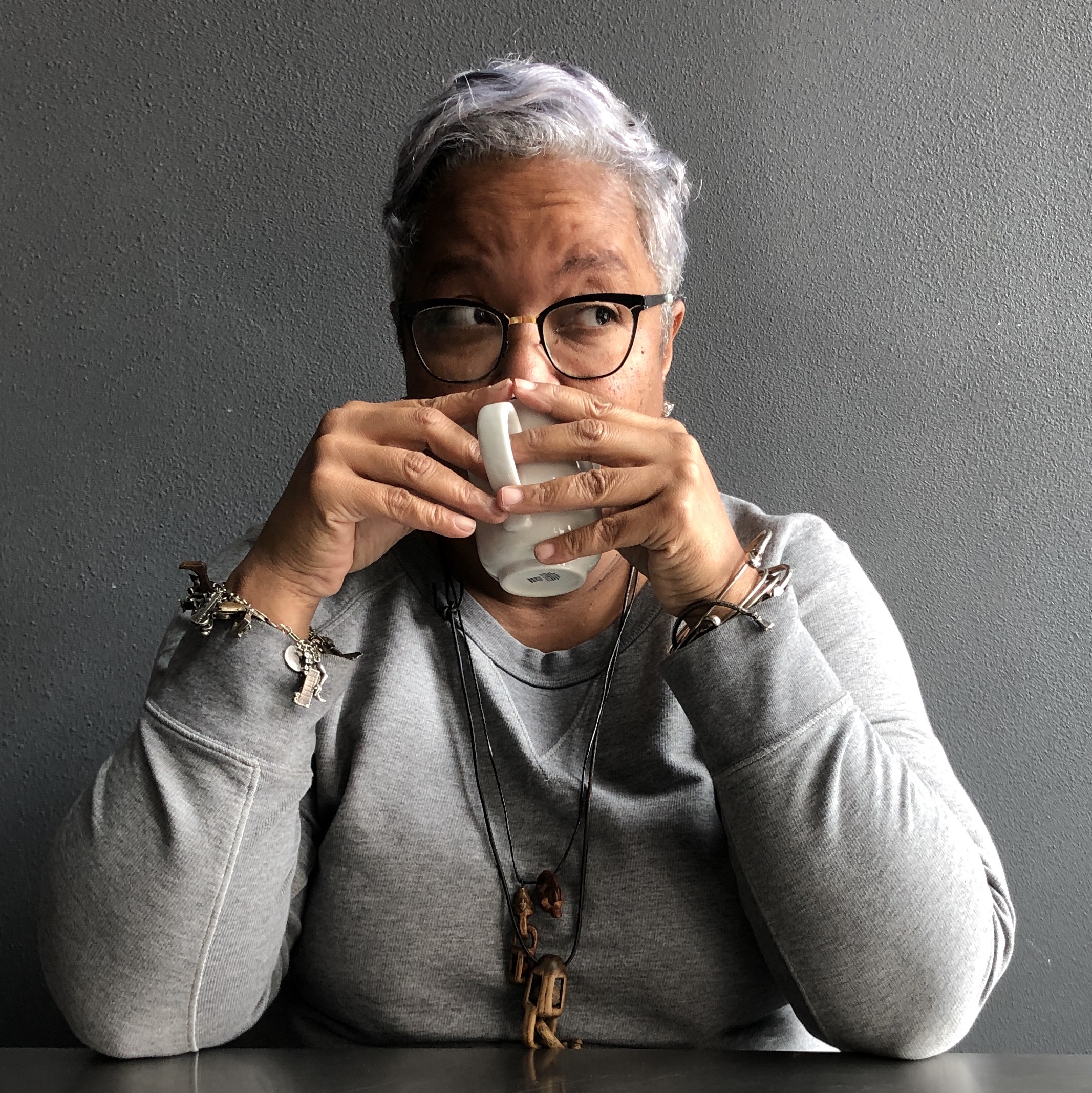A woman with short white hair and black glasses, holding a mug.