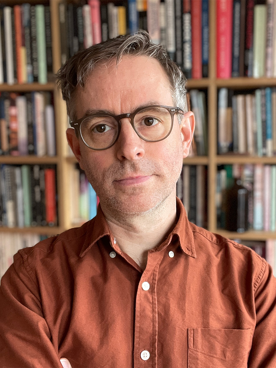 A man with graying hair and round brown glasses, wearing a button down shirt.
