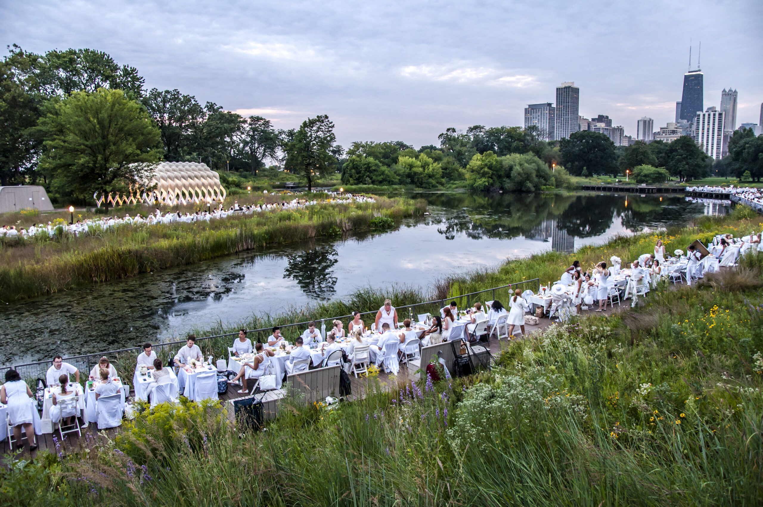 people dressed all in white along seated at a long table along a waterway