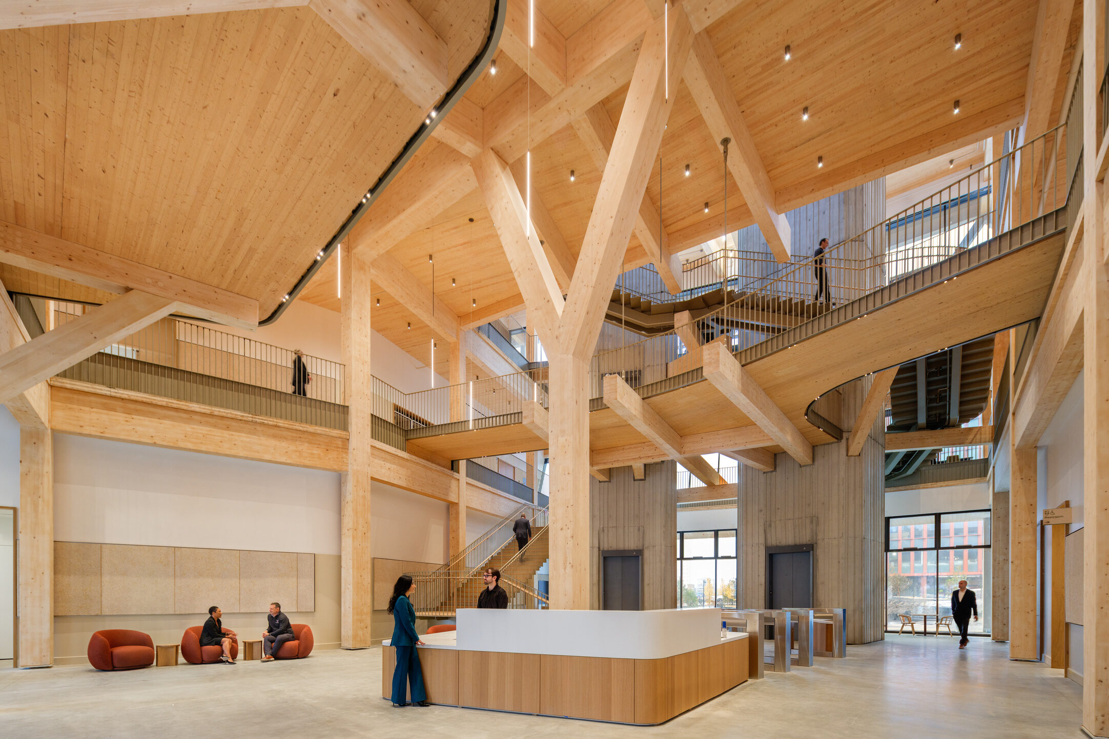 Woodframe interior of a building's open atrium space with people at a central desk and in chairs