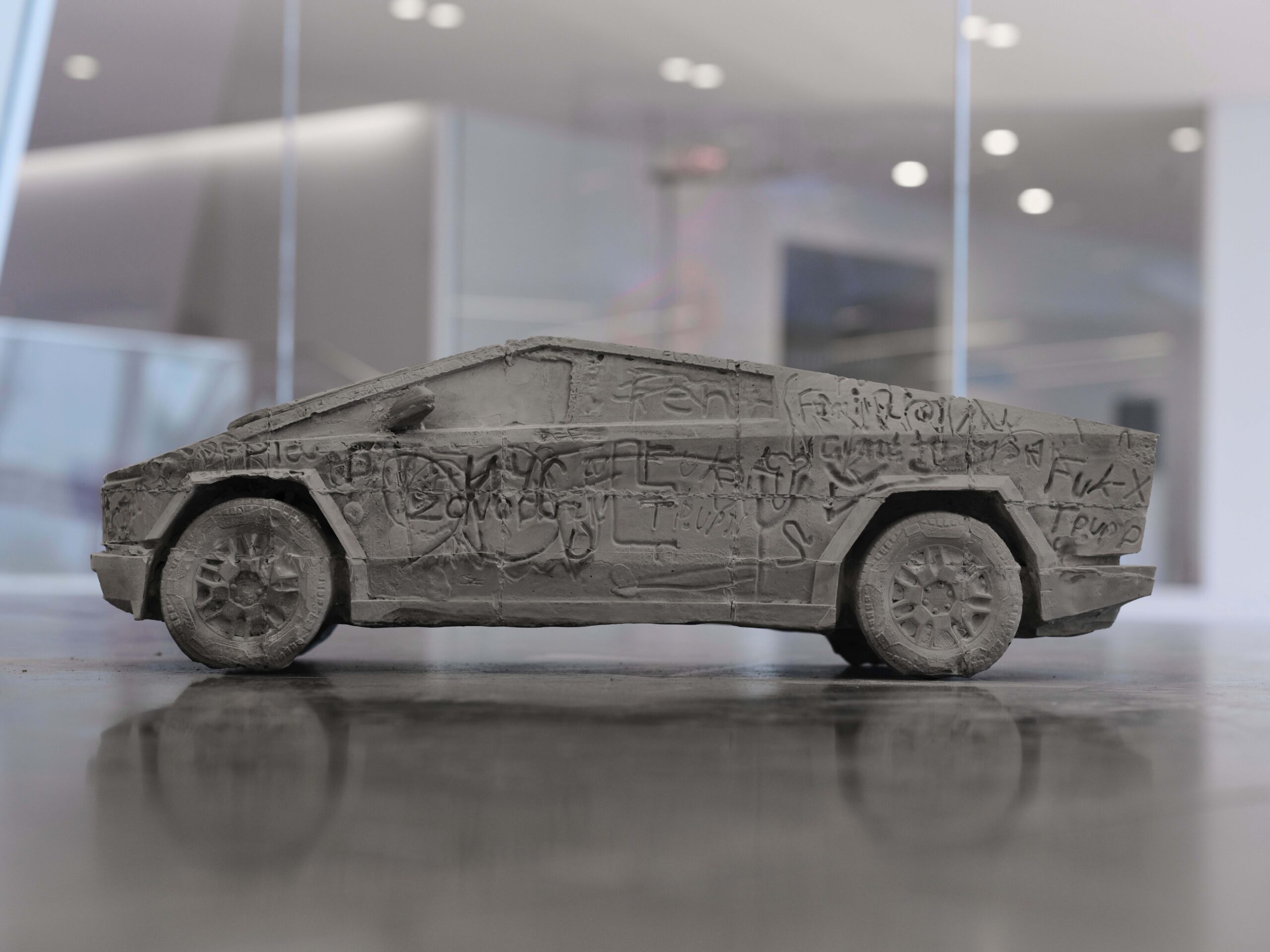 A small car made of clay or concrete with scribbles and writings on its surface.